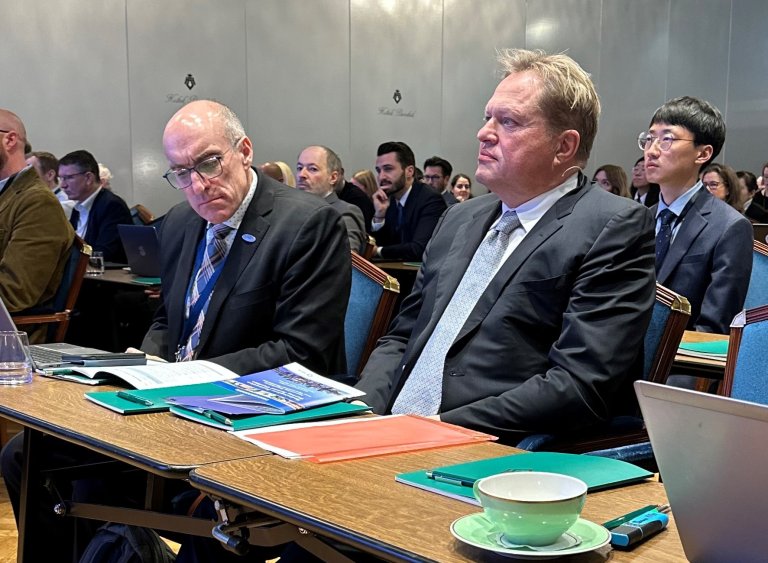 Menn i dress lytter til foredrag.