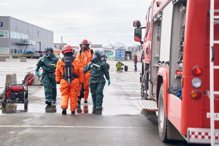En brannbil og fire personer i vernedrakter og med gassmaske.
