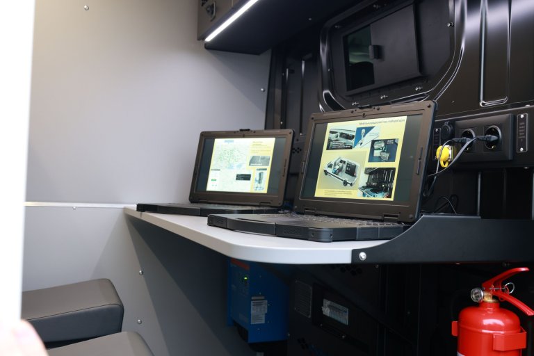 To skjermer med bilder på en pult, fra innsiden av en varebil.