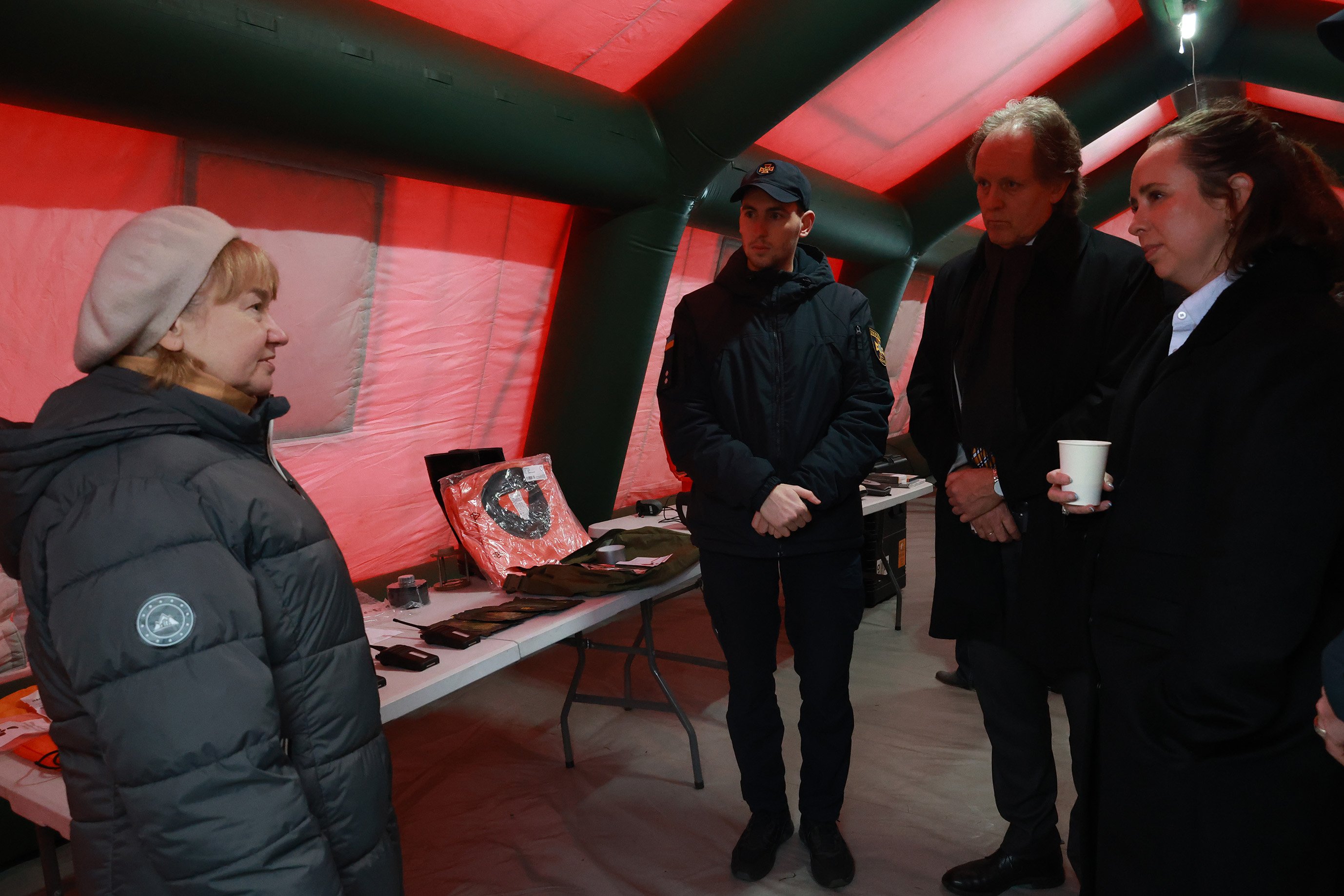 Fire personer inne i et rødt telt, med utstyr liggende på et bord bak.